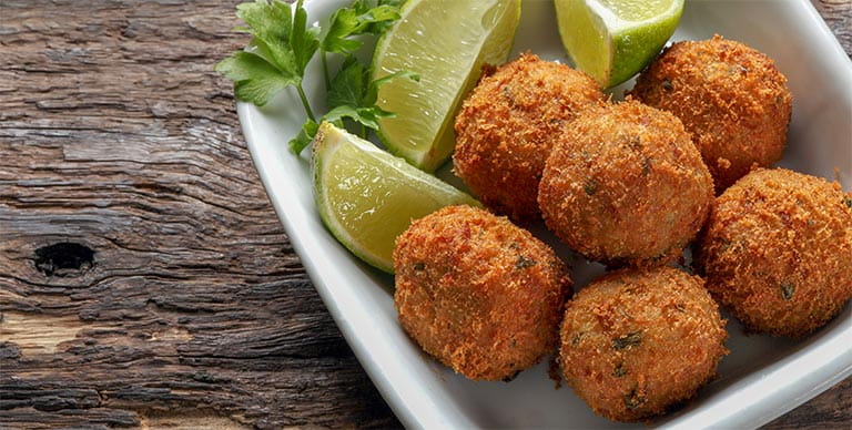 Traditional Caribbean cod fritters in a bowl on a table, with wedges of lime